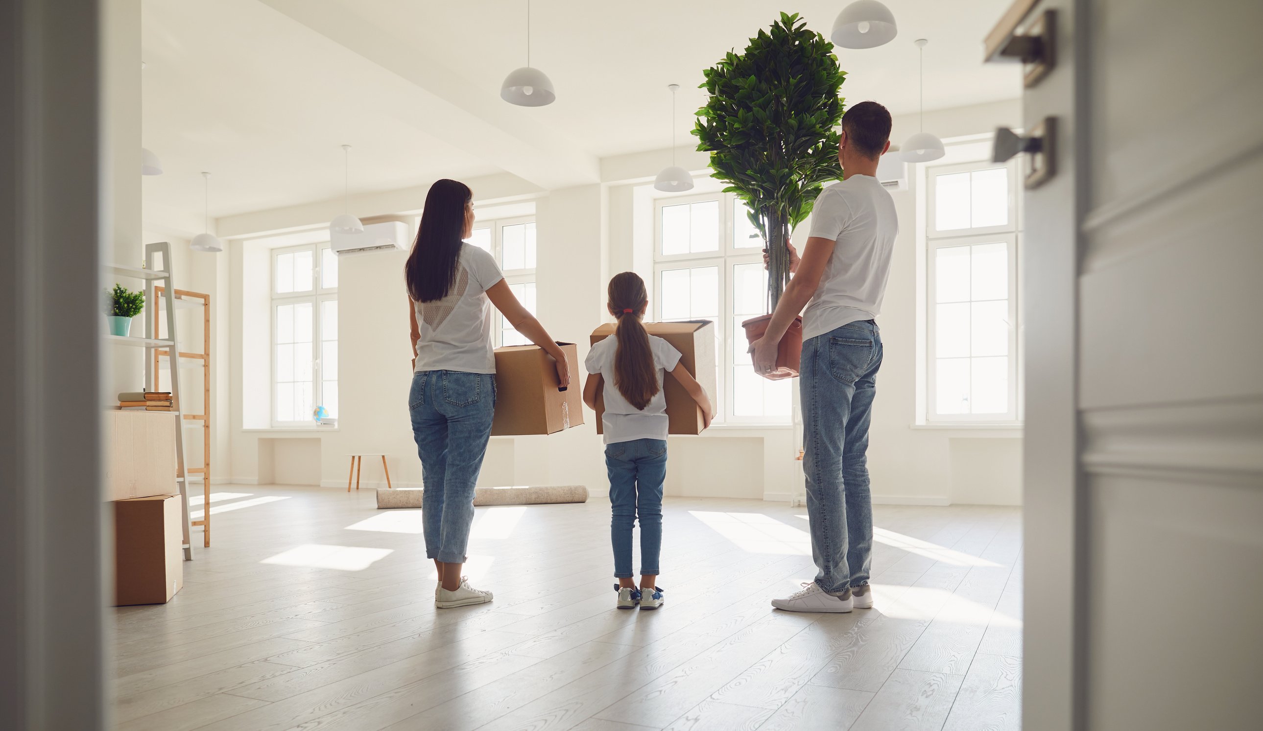 Happy Family with Children Moving with Boxes in a New Apartment House. Back View.